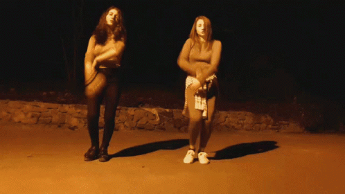 two women stand in a darkened area with each holding a cellphone