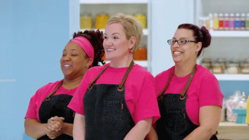 three ladies are wearing aprons in a kitchen