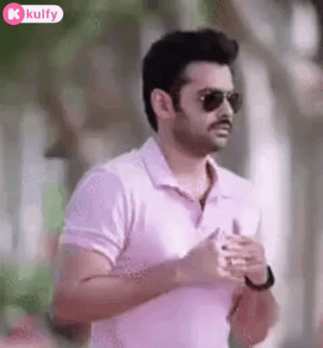 a man with sunglasses on walking and wearing a pink shirt