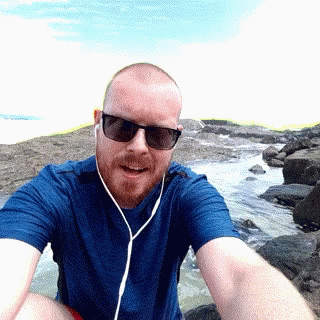 man with blue headphones sitting on rocks at beach