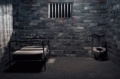 a dark prison cell area with a bed and  bars
