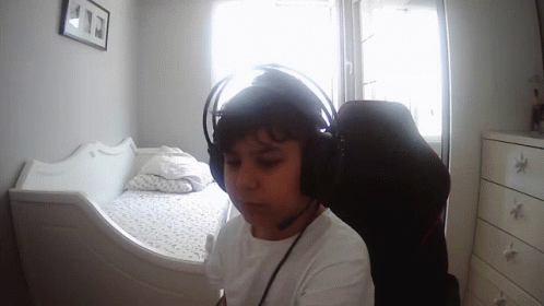 a boy wearing headphones and white shirt sitting in front of a bed