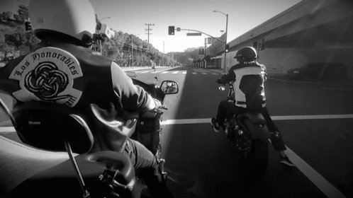 two people wearing helmets while riding motorcycles on a city street