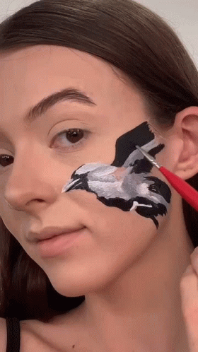 a woman is holding a paintbrush while painting the face of a animal