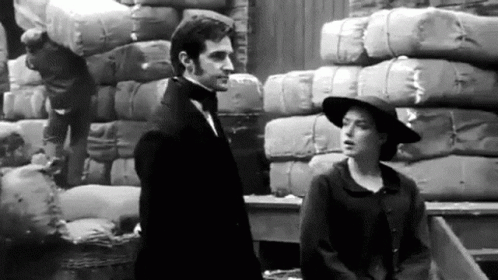 a man standing next to a woman in front of stacks of hay