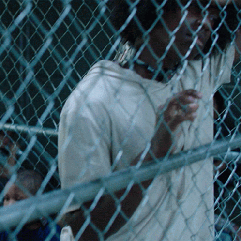 man in baseball uniform looking through a chain link fence