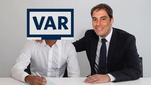 two men with blue faces sit behind a white sign that says var
