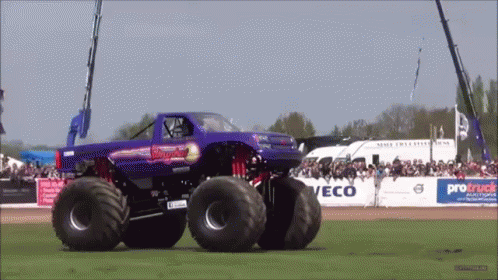 a red truck with big wheels driving across a dirt field