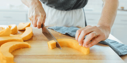 a woman in white apron slicing blue dough