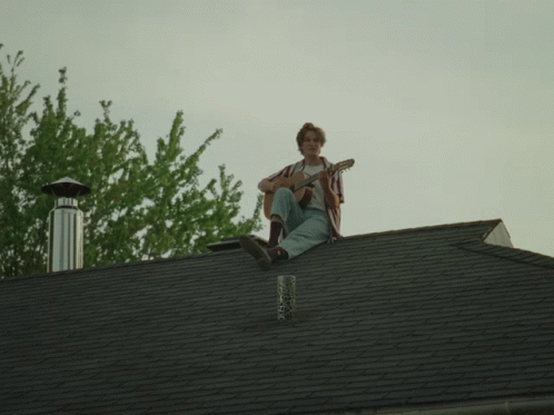 a man sitting on top of a roof playing the guitar