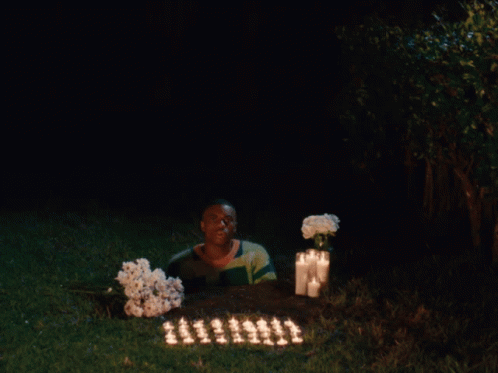 a person sitting on the grass in the dark with candles in front of them