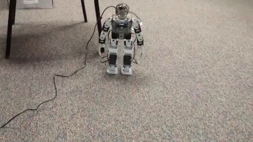a small robot standing next to two large desks