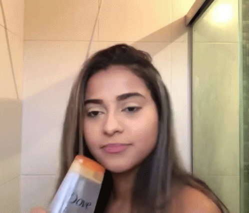 a girl holding a container of soap and blow drying her hair