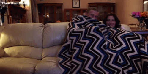 a man and woman laying on a couch under a blanket