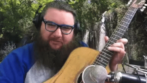 a bearded man with glasses is holding a blue guitar and is making an expression of shock