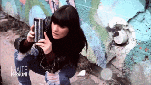 a girl in blue makeup stands leaning against a wall holding a boombox