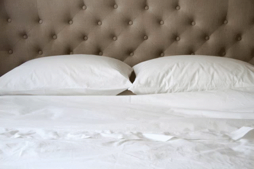 a white bed topped with two pillows and a headboard
