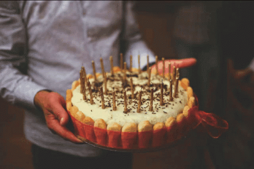 a hand in a glove holding a cake that is decorated with candles