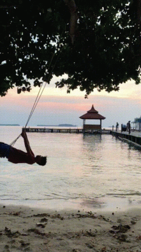 a person is hanging off of a swing in the air by water