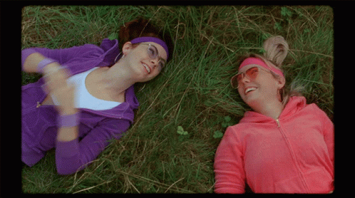 two women wearing purple laying on grass in the sun