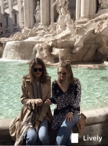 two young ladies are sitting by the fountain of some sort