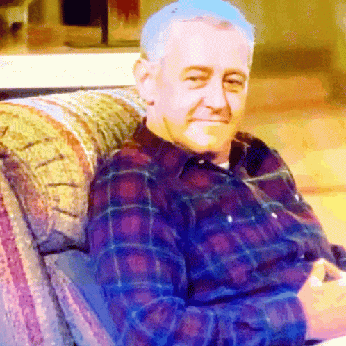 an older man in red shirt sitting on a couch