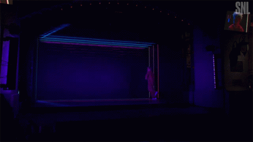 a dimly lit stage with curtains and a person walking by