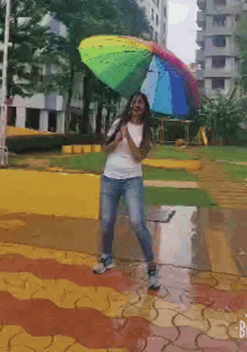 woman holding rainbow colored umbrella while standing on paved area