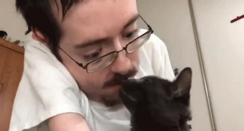 a man with glasses kissing a small black cat