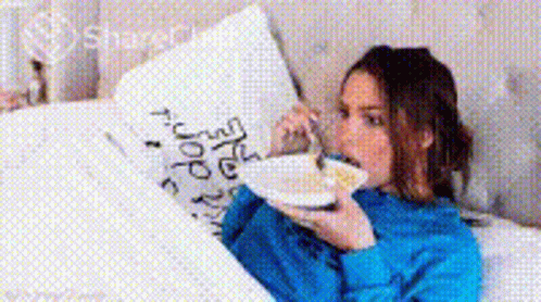a woman holding a white cup in her mouth while lying on a bed
