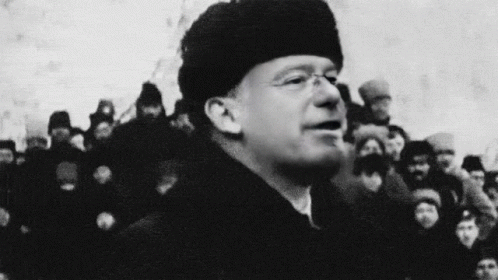 black and white pograph of man wearing beanie speaking with many people in background