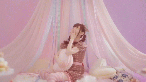 an asian girl sitting on top of a bed with a pink canopy