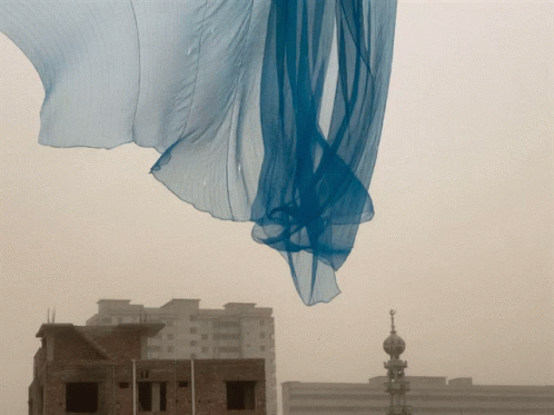 a long white cloth hangs over buildings in a hazy sky