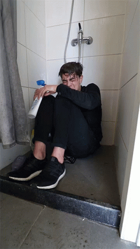 a man with blue hair sitting on the floor in front of the shower