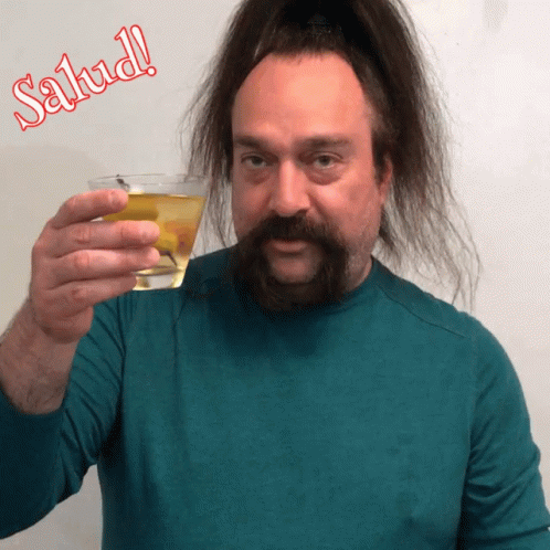 there is a man with long hair and green shirt holding up a glass of liquor