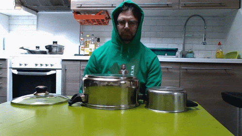 a man wearing a green sweatshirt and hood on with silver pots behind him
