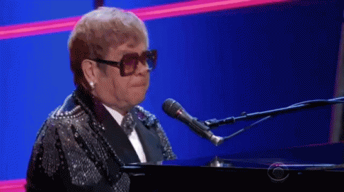 a man wearing glasses and a black jacket stands at a piano