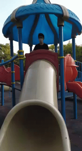 a man is sitting in the seat of a slide at a playground