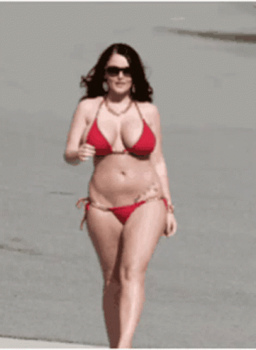 a woman walking along the beach while wearing a bikini top