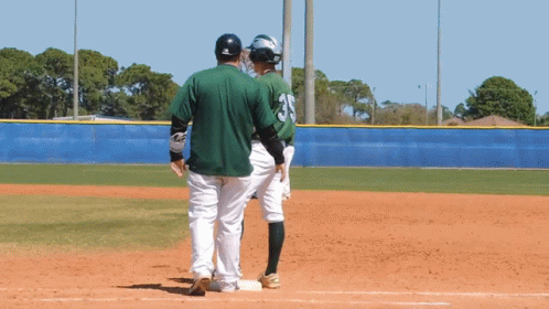 two baseball players, one wearing a green jersey, standing near a base