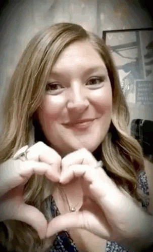 a woman with long hair and glasses making a heart sign