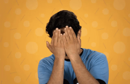 man covering face with hands with blue background