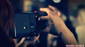 two hands holding a black camera in front of a tv screen