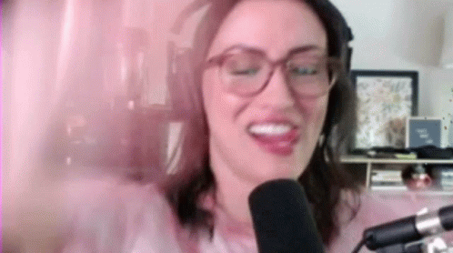 a woman with glasses and purple makeup has an mic in front of her