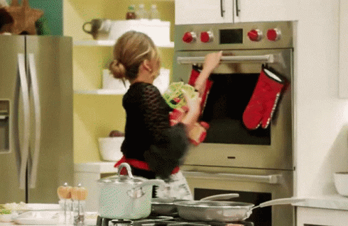 a woman wearing black using an oven mitt to open the oven