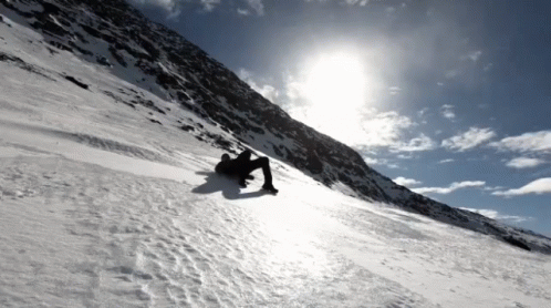 snowboarder descending down a steep snowy mountain with sun shining in the background