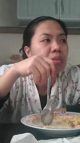 woman holding spoons to her chin sitting at a table