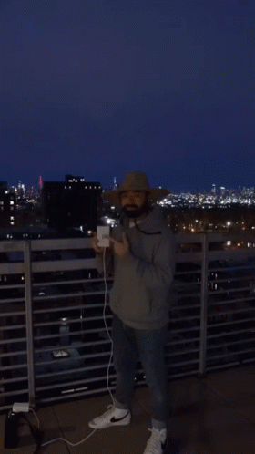man taking a picture on top of roof overlooking city at night