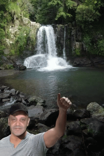 a man standing in front of a waterfall holding a phone
