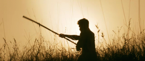 man holding an arrow and a gun standing in the grass